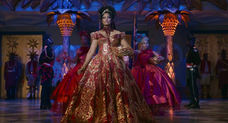 Coming 2 America royal entrance in a red and gold gown beneath lit palm columns