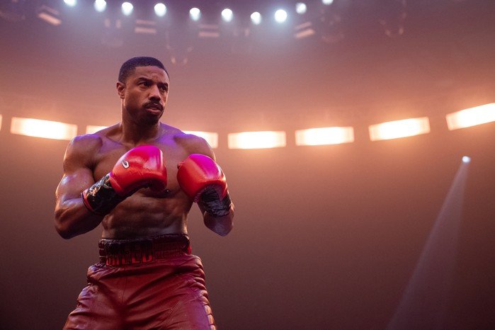 Creed 3 boxer in red gloves under arena ring lights