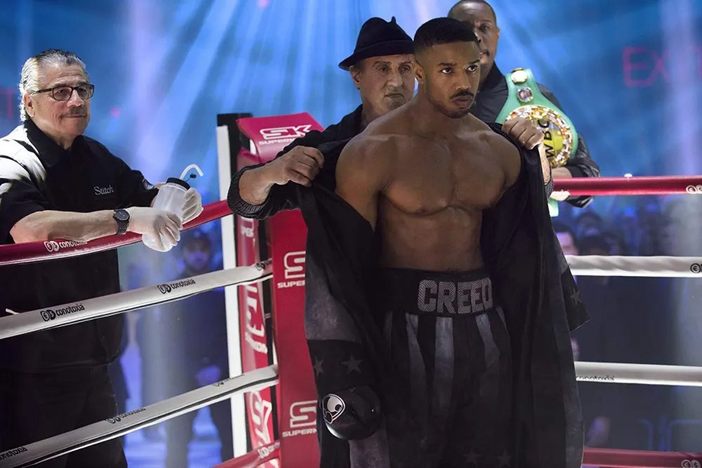 Creed fighter and corner team in the ring under blue arena lighting