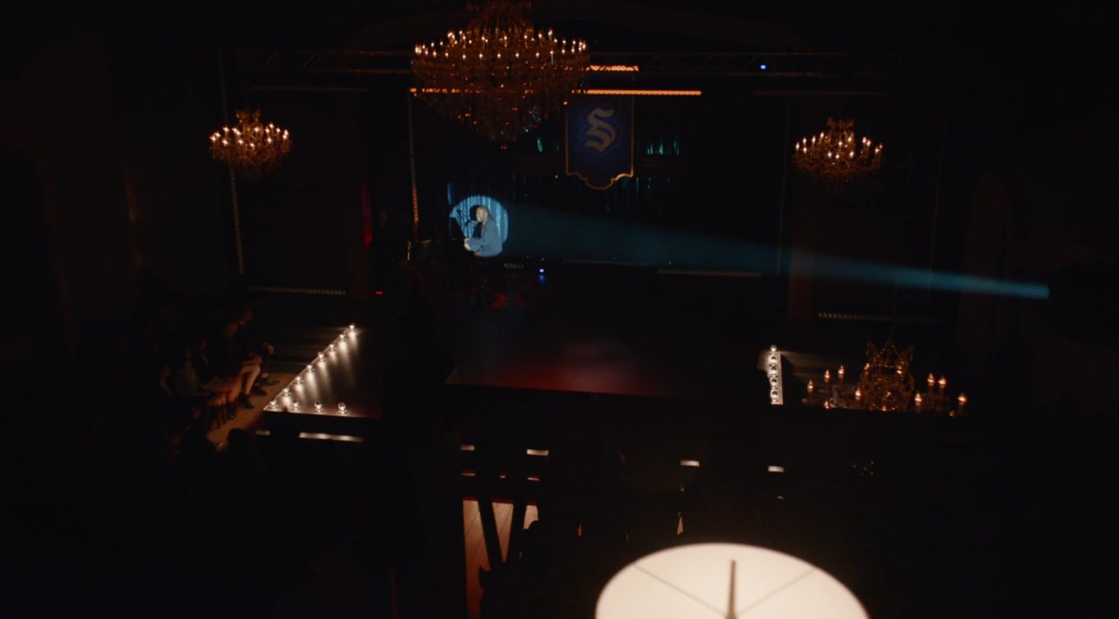 Legacies aerial performer above warm amber light lines and glass globes