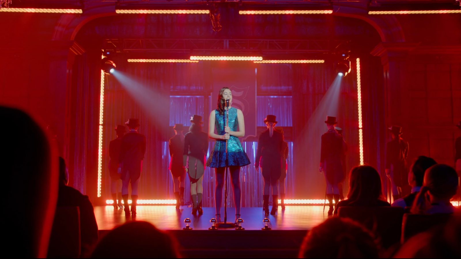 Legacies ballroom stage with chandeliers and glowing floor lines around a lone singer