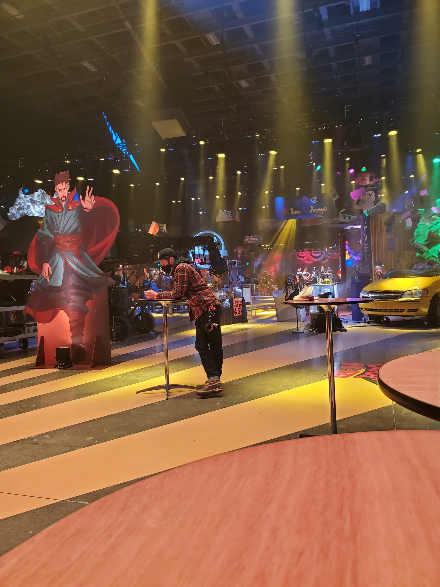 Ms. Marvel Season 1 AvengerCon set on stage, with yellow beams over a striped floor and a camera operator at work